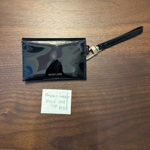 Hayden Lasher black patent card case with metal bow and strap.